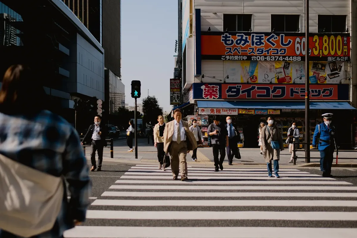 A bustling city intersection in Japan with diverse pedestrians crossing a zebra crossing.