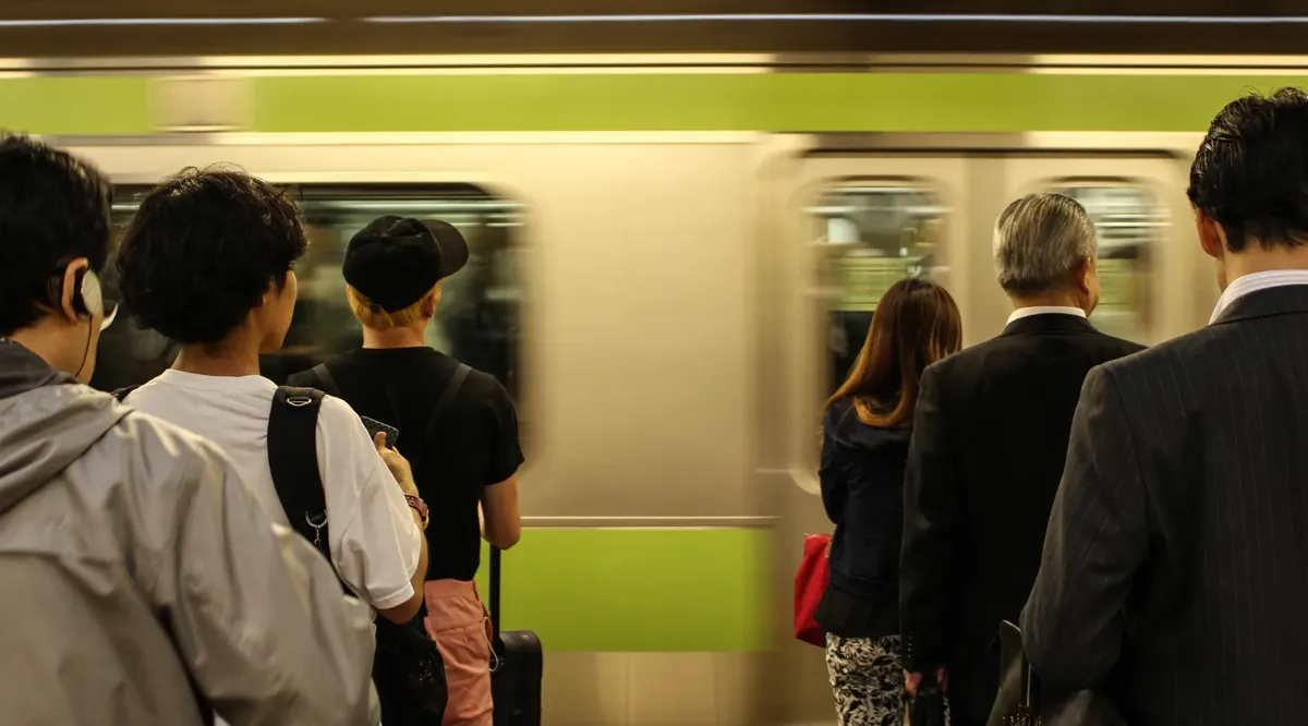 Passengers waiting as a train speeds through a station in Japan, capturing daily commute moments.