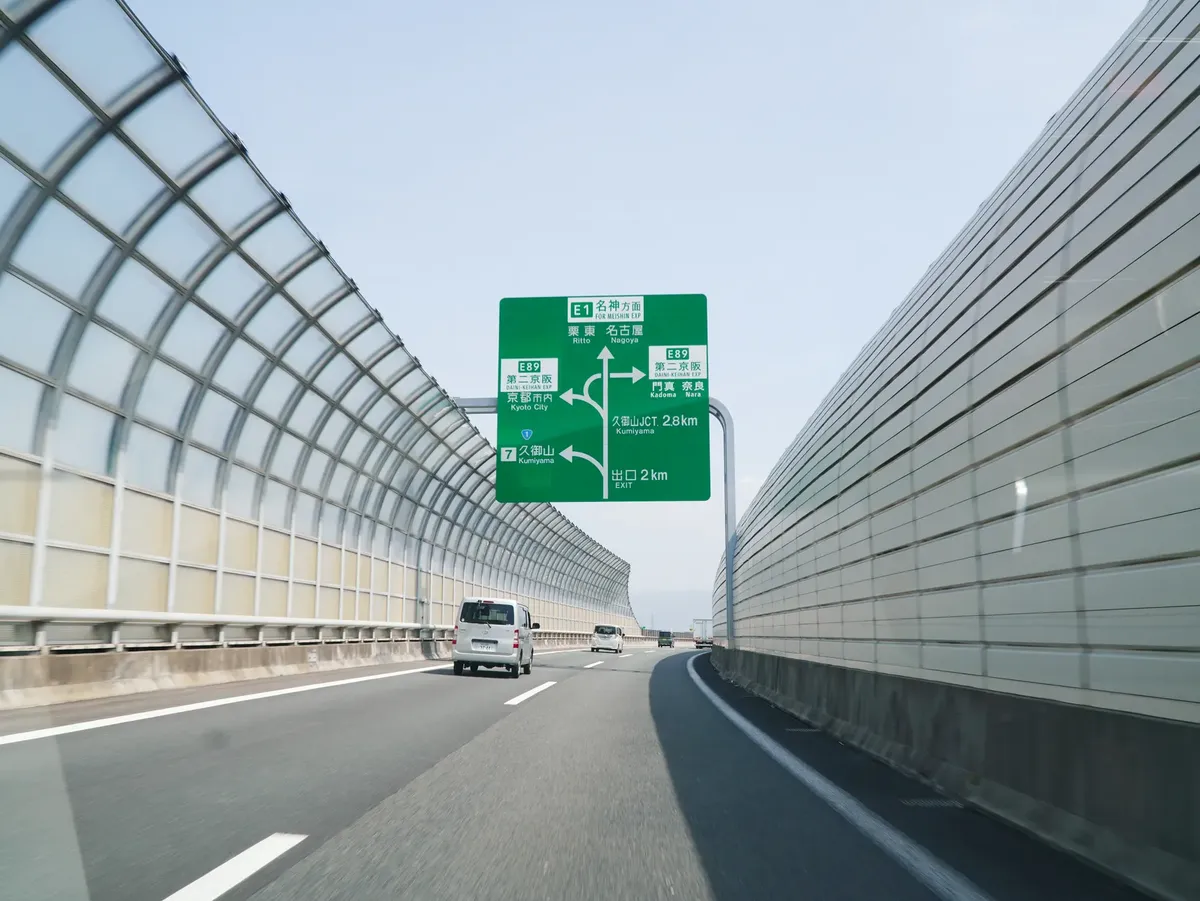 Wide highway with green directional sign and cars traveling in urban Japan.