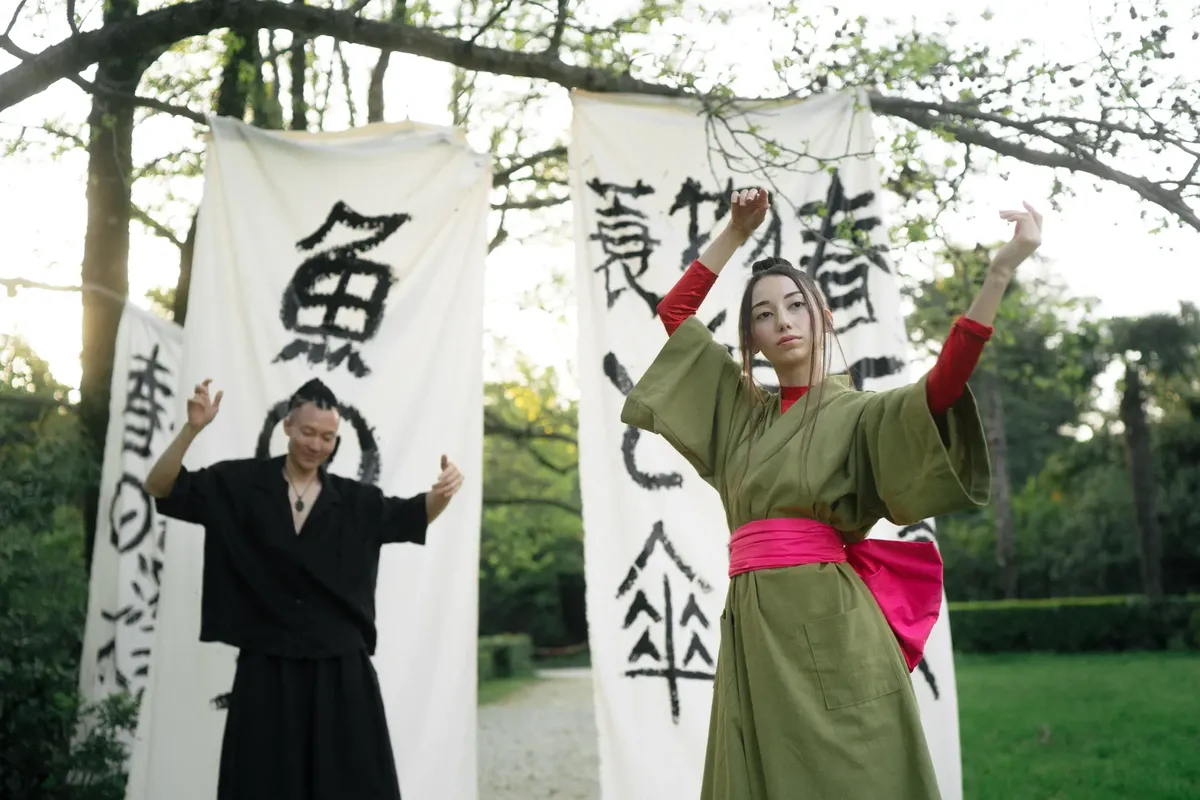 Two people performing a traditional Japanese dance outdoors with calligraphy banners in the background.