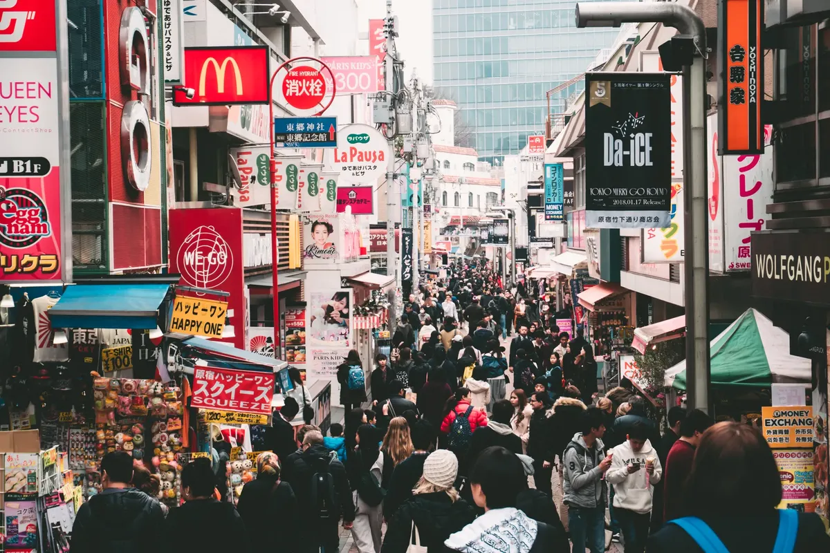 Vibrant daytime street market in Tokyo, crowded with shoppers and colorful signage.