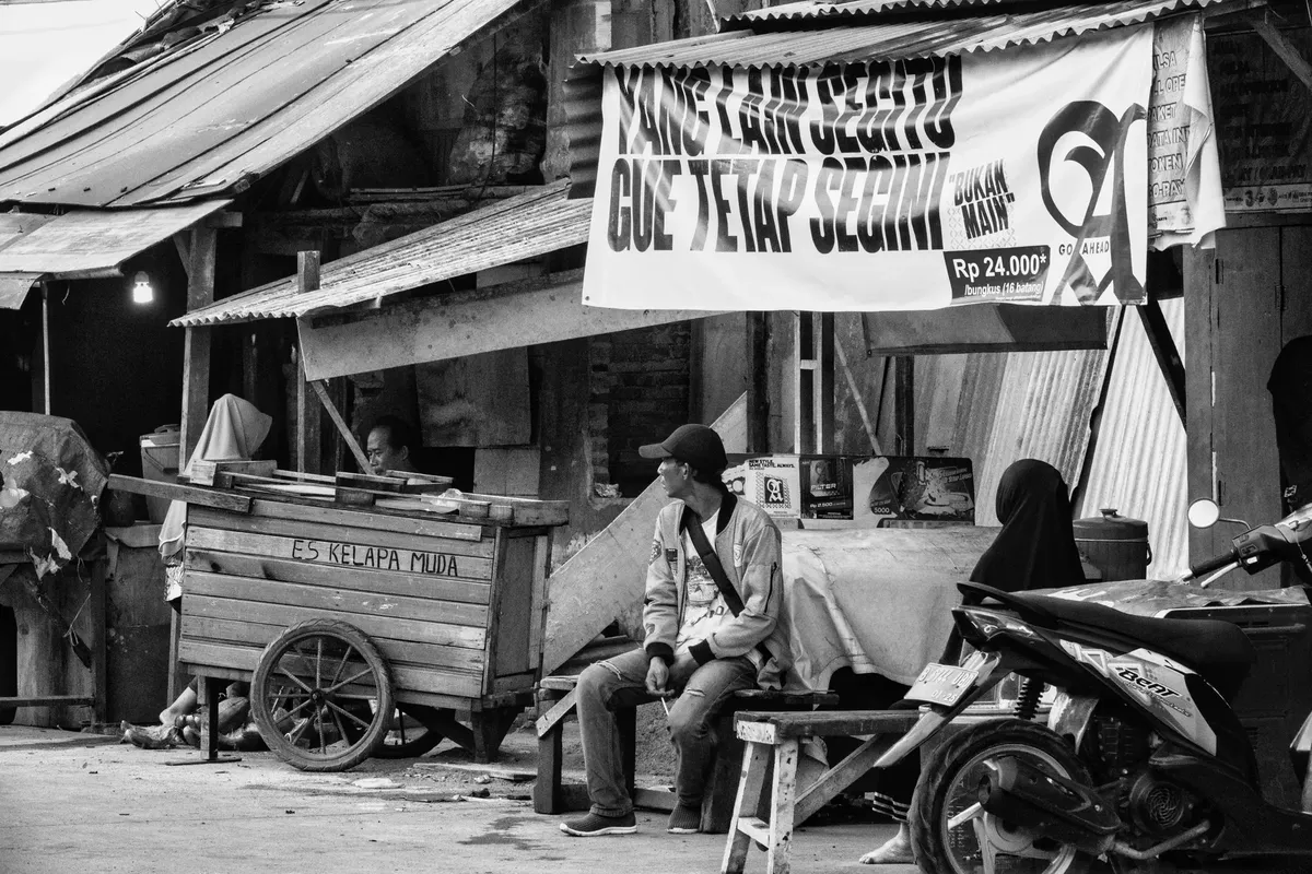 Black and white street scene in Jakarta showcasing local life with food stalls and people.